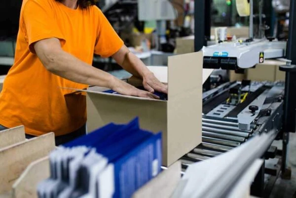 Worker packing products into a cardboard box on an automated manufacturing production line