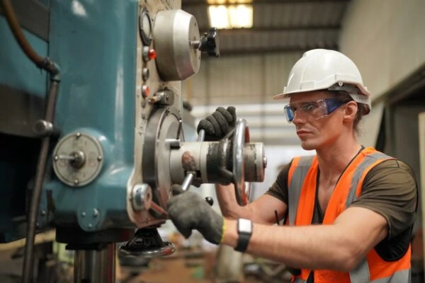 : Skilled industrial technician recruited by Alsaqib operating heavy machinery while wearing protective safety equipment.